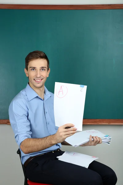 Jonge leraar zitten in de buurt van schoolbord in school klas — Stockfoto