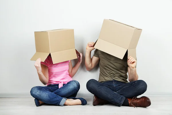 Couple with cardboard boxes on their heads sitting on floor near wall — Stock Photo, Image