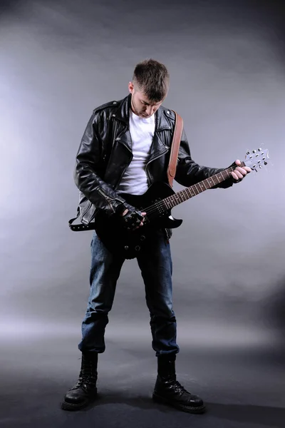 Молодой музыкант играет на гитаре на сером фоне — стоковое фото