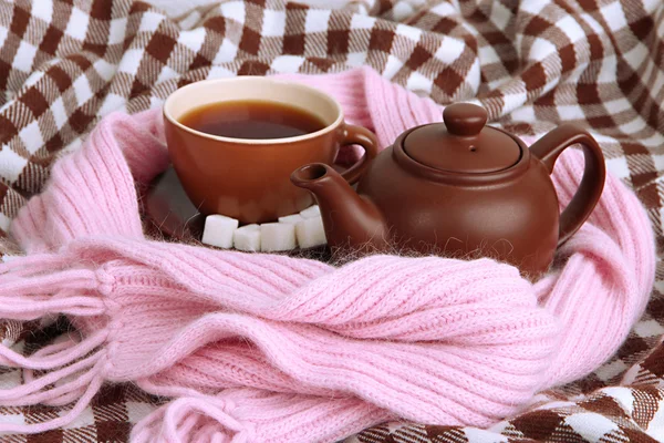 Tasse und Teekanne mit Schal auf Stoffhintergrund — Stockfoto