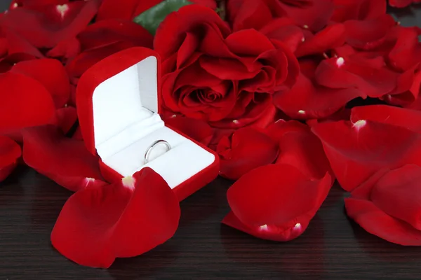 Ring surrounded by rose petals on wooden table close-up — Stock Photo, Image