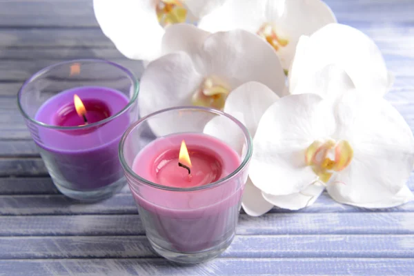 Hermosas velas de colores y flores de orquídea, sobre mesa de madera de color, sobre fondo claro — Foto de Stock