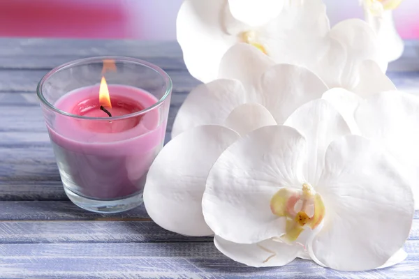 Hermosas velas de colores y flores de orquídea, sobre mesa de madera de color, sobre fondo claro — Foto de Stock