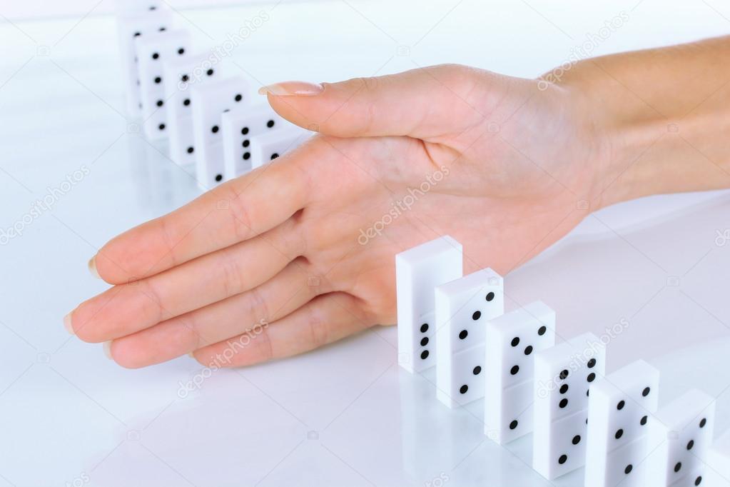 Hand stopping dominoes falling isolated on white