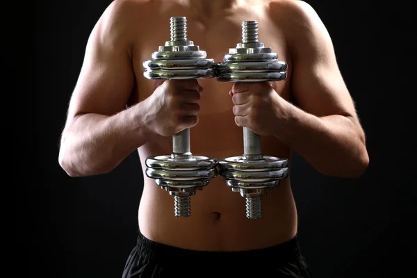 Handsome young muscular sportsman execute exercise with dumbbells on dark background — Stock Photo, Image