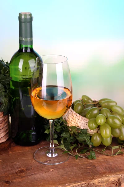 Maturare uva verde e viola in cesto con vino su tavolo di legno su sfondo brillante — Foto Stock