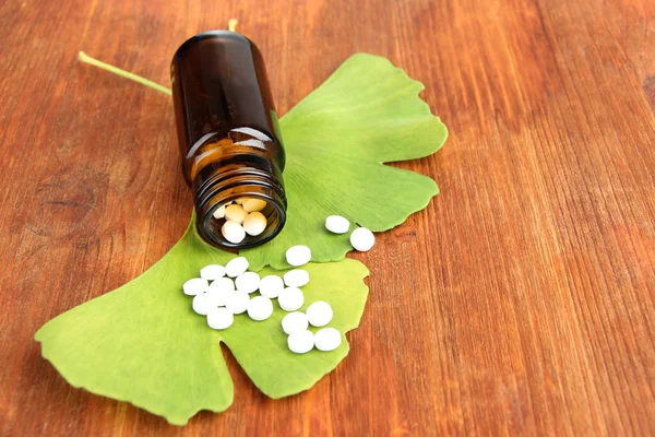 Feuilles de ginkgo biloba et bouteille de médicament sur fond en bois — Photo