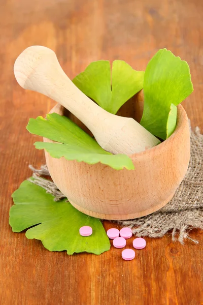 Ginkgo biloba leaves in mortar and pills on wooden background — Stock Photo, Image