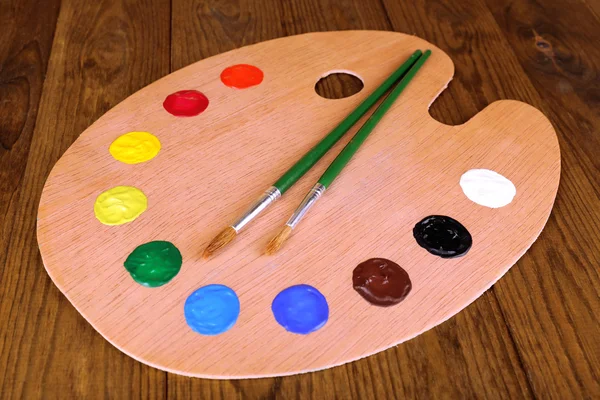 Wooden art palette with paint and brushes on table close-up — Stock Photo, Image