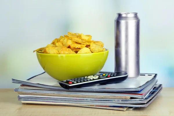 Chips dans le bol, la bière et la télévision à distance sur une table en bois sur fond de pièce — Photo