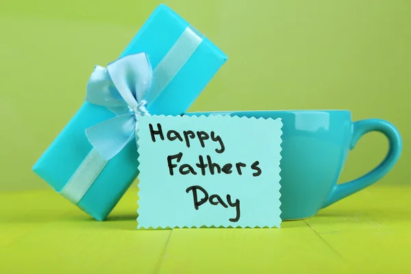 Happy Fathers Day tag with gift box and cup, on wooden table, on light background — Stock Photo, Image