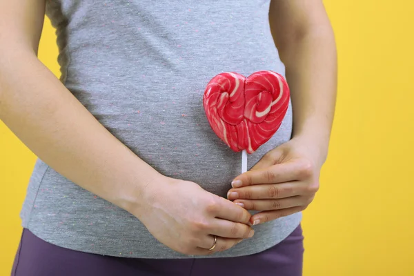 Donna incinta in possesso di lecca-lecca rosso su sfondo giallo — Foto Stock