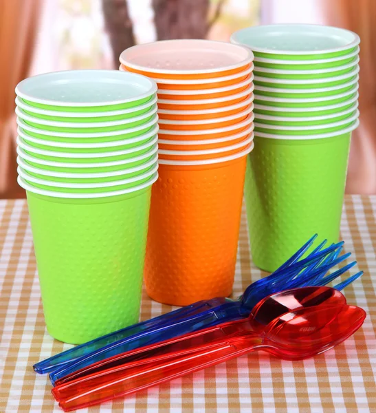 Tasses en plastique, cuillères de différentes couleurs sur fond lumineux — Photo