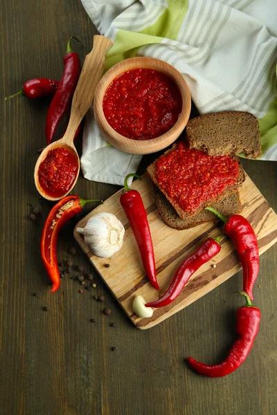 Composizione con salsa su pane, peperoncino rosso e aglio, su tovagliolo, su fondo di legno — Foto Stock