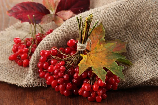 Red berries of viburnum on sackcloth napkin, on wooden background — Stock Photo, Image