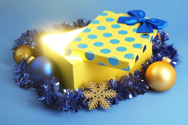Scatola regalo con luce brillante su di esso su sfondo blu — Foto Stock