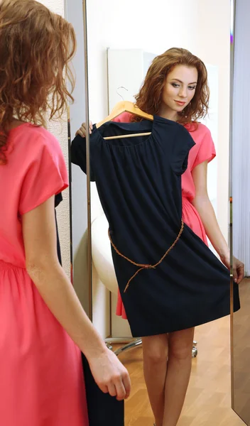 Beautiful girl trying dress near mirror in room — Stock Photo, Image