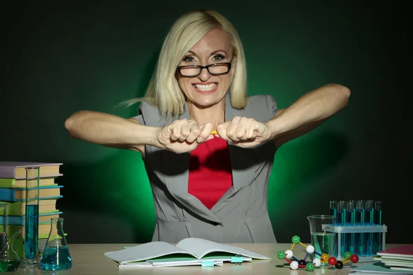 Wicked scheikunde leraar zittend aan tafel op donkere kleurrijke achtergrond — Stockfoto