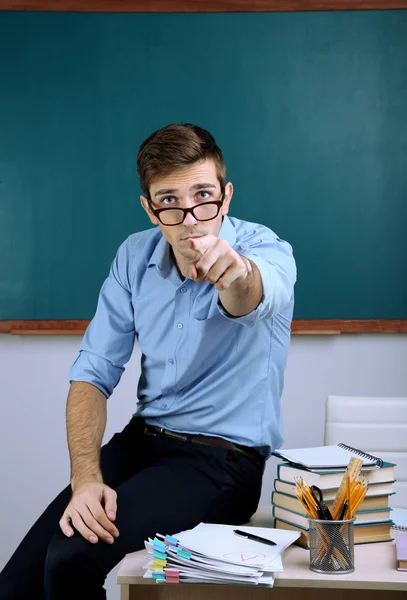 Joven profesor sentado en el escritorio en el aula de la escuela — Foto de Stock