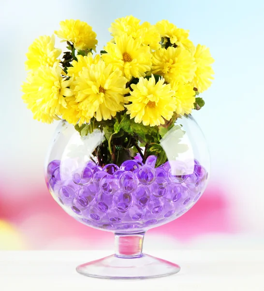 Hermosas flores en jarrón con hidrogel en la mesa sobre fondo brillante —  Fotos de Stock