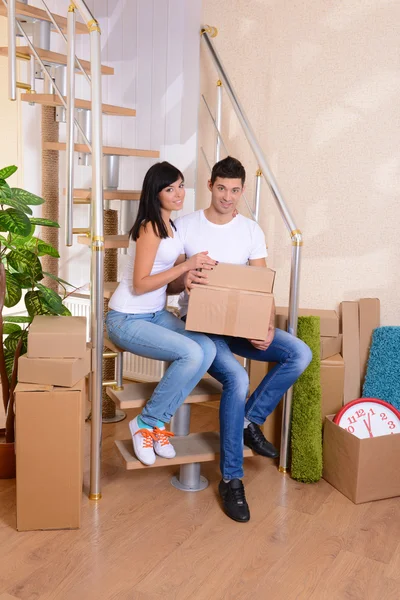 Jovem casal com caixas em nova casa no fundo escada — Fotografia de Stock