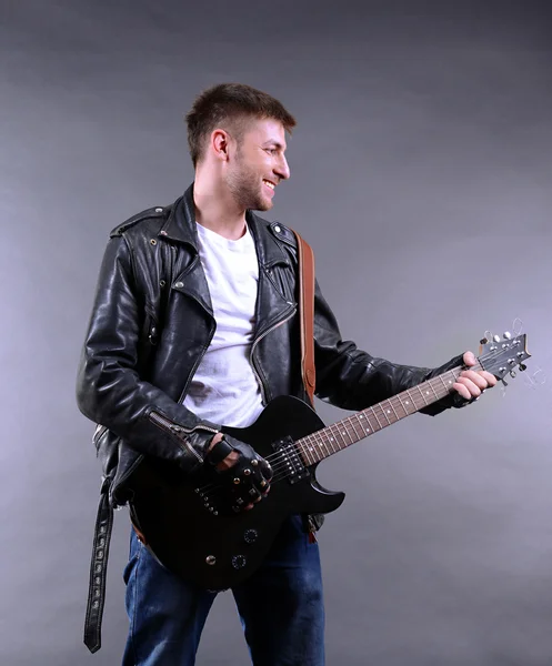 若い音楽家の灰色の背景でギターを弾く — ストック写真