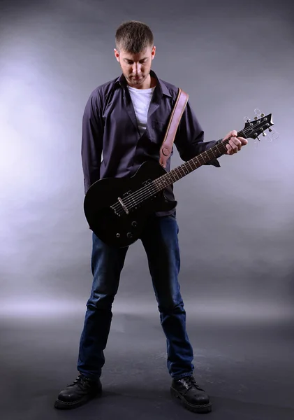 Jovem músico tocando guitarra em fundo cinza — Fotografia de Stock
