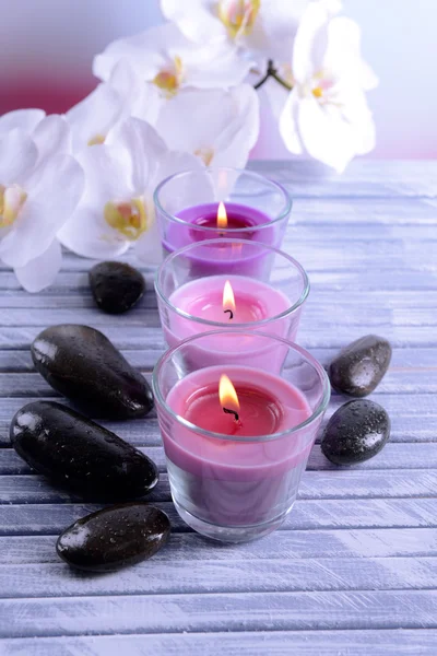 Velas coloridas bonitas, pedras do spa e flor do orchid, na tabela de madeira da cor, no fundo claro — Fotografia de Stock