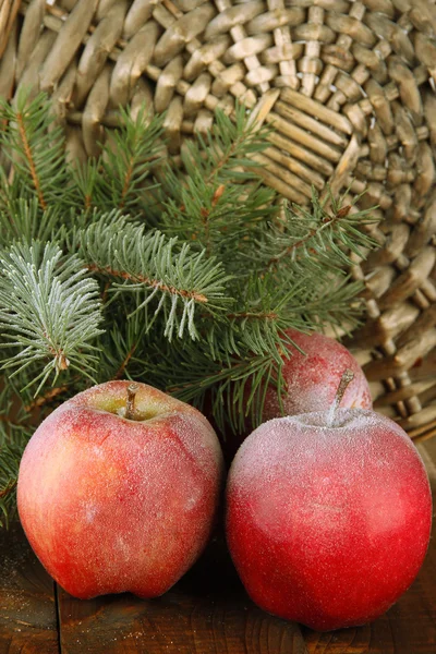 Red frosted apples with fir branch on table on wicker background — Stock Photo, Image