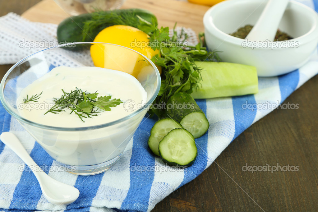 Cucumber yogurt in glass bowl, on color napkin, on wooden background