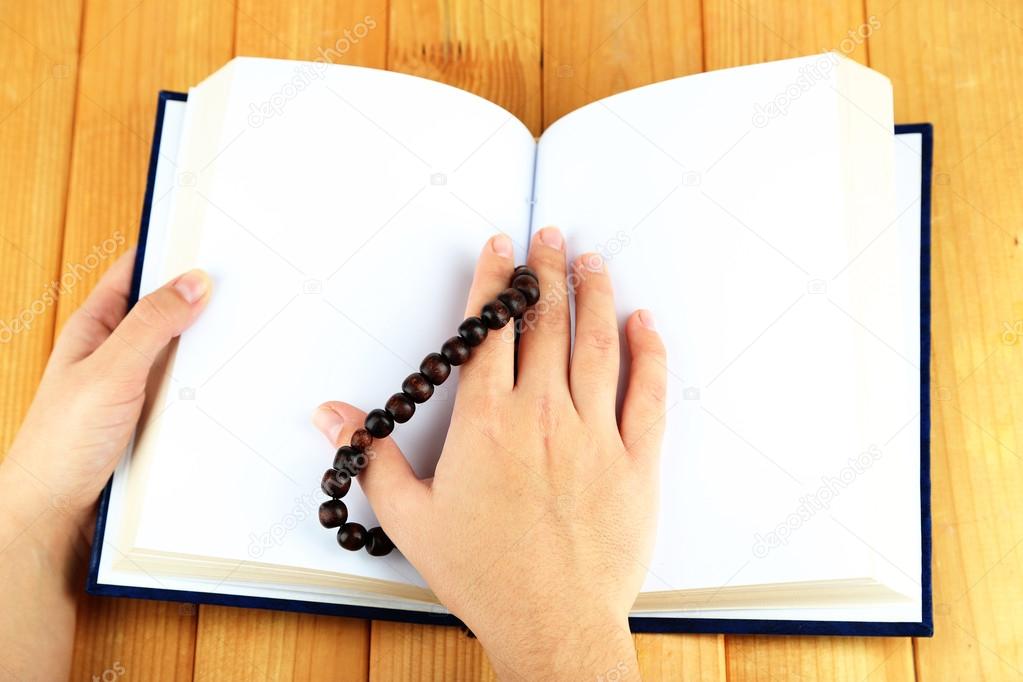 Hands with rosary and holy book, on light background