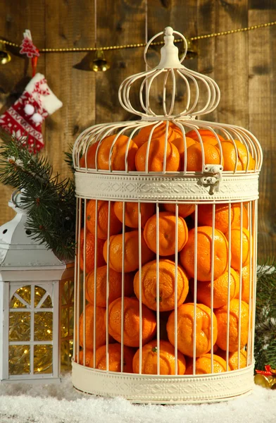 Tangerines in decorative cage with Christmas decor, on wooden background — Stock Photo, Image
