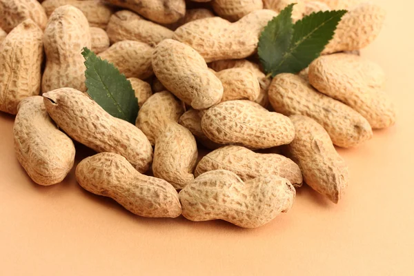 Tasty peanuts with green leaves, on beige background — Stock Photo, Image