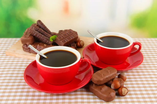 Tazas rojas de café fuerte con barras de chocolate en mantel sobre fondo brillante — Foto de Stock