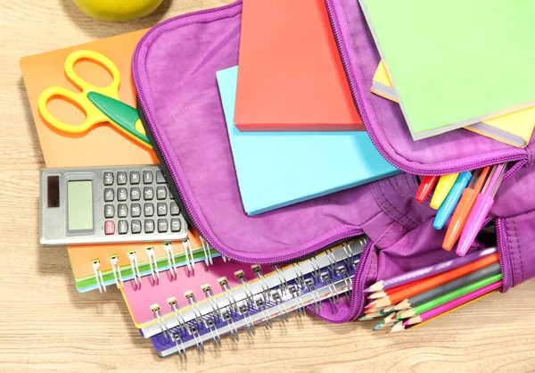 Purple backpack with school supplies on wooden background — Stock Photo, Image