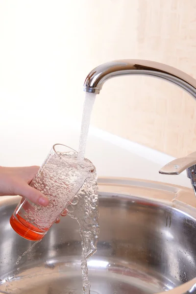 Hand som håller glas vatten hälls från köksblandare — Stockfoto
