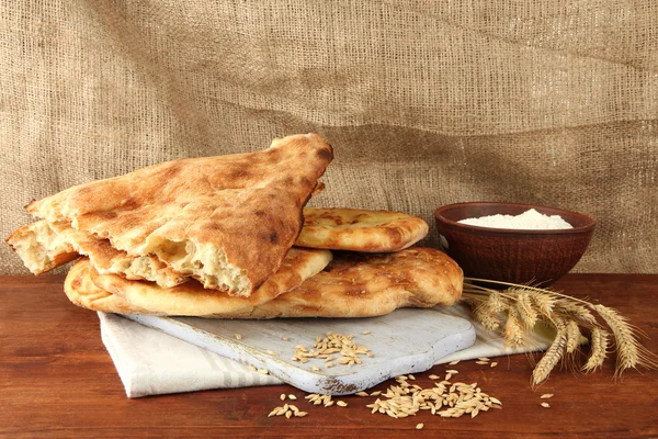 Pães Pita com picos e farinha na mesa sobre fundo de pano de saco — Fotografia de Stock