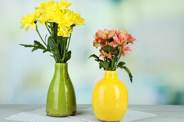 Hermosas flores en jarrones, sobre mesa de madera, sobre fondo claro — Foto de Stock
