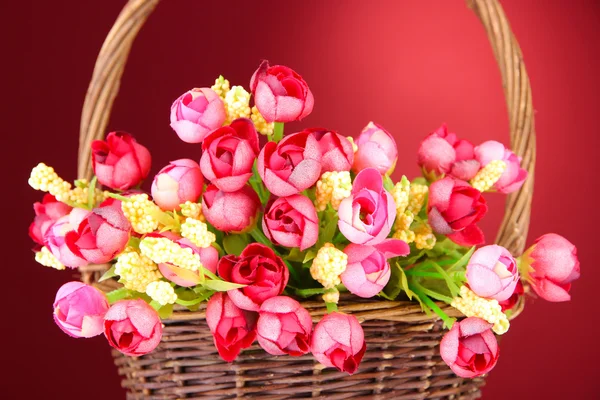 Bukiet pięknych kwiatów sztucznych w wiklinowym koszu, na czerwonym tle — Zdjęcie stockowe
