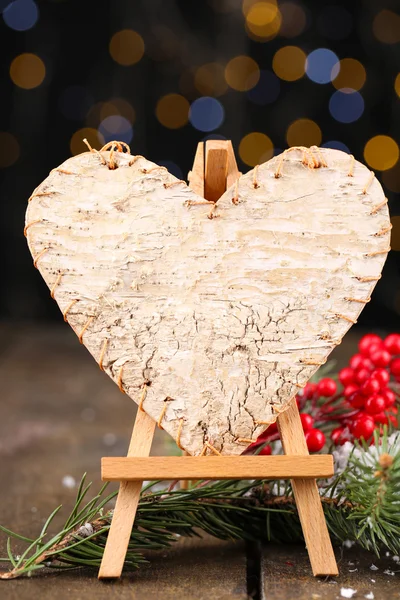 Corazón decorativo sobre caballete, sobre mesa de madera, sobre fondo brillante — Foto de Stock