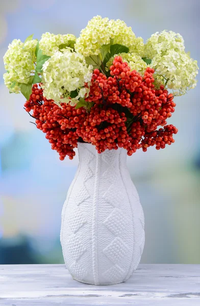 Blommor och bär i vas, på träbord, på ljus bakgrund — Stockfoto