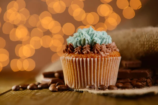 Gustoso cupcake con crema di burro, su tavolo di legno, su fondo luci — Foto Stock