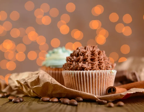 Cupcakes saborosos com creme de manteiga, na mesa de madeira, no fundo luzes — Fotografia de Stock