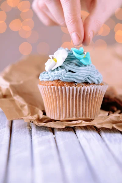 Cupcake saboroso com creme de manteiga, na mesa de madeira cor, no fundo luzes — Fotografia de Stock