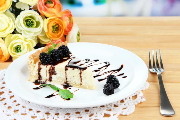 Slice of cheesecake with chocolate sauce and blackberry on plate, on wooden table, on bright background — Stock Photo, Image
