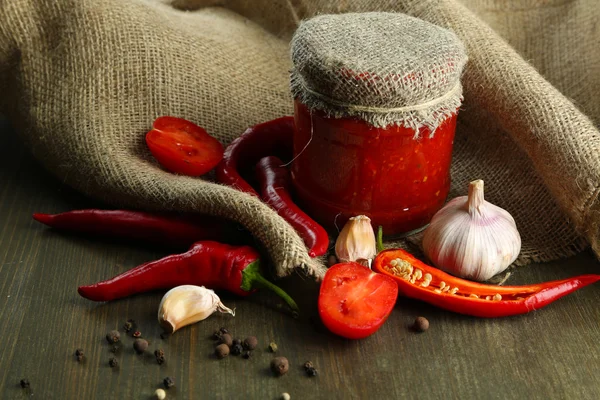 作文与莎莎酱在玻璃罐、 红辣椒和大蒜上麻布，木制背景上 — 图库照片