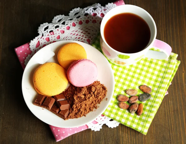 Cacao en taza con dulces y cacao en polvo en plato sobre mesa de madera —  Fotos de Stock