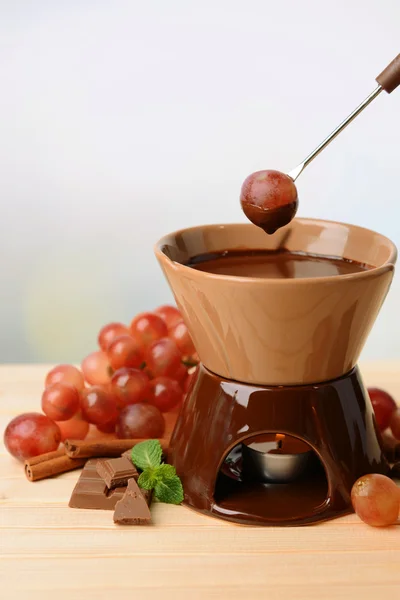 Шоколадний фонтан з фруктами, на дерев'яному столі, на світлому фоні — стокове фото