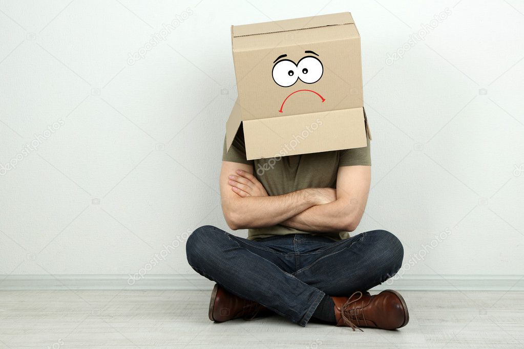 Man with cardboard box on his head sitting on floor near wall