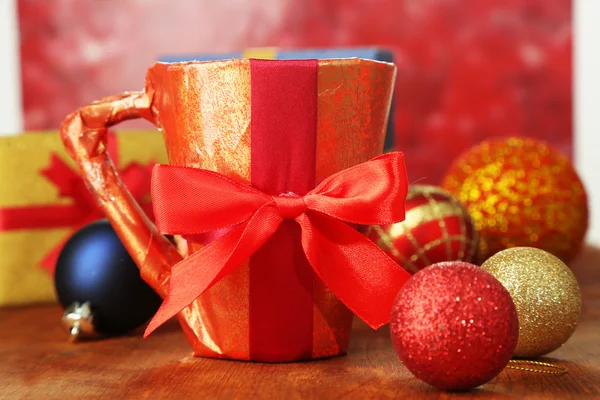 Copa envasada en papel de regalo con regalos en mesa de madera sobre fondo brillante — Foto de Stock